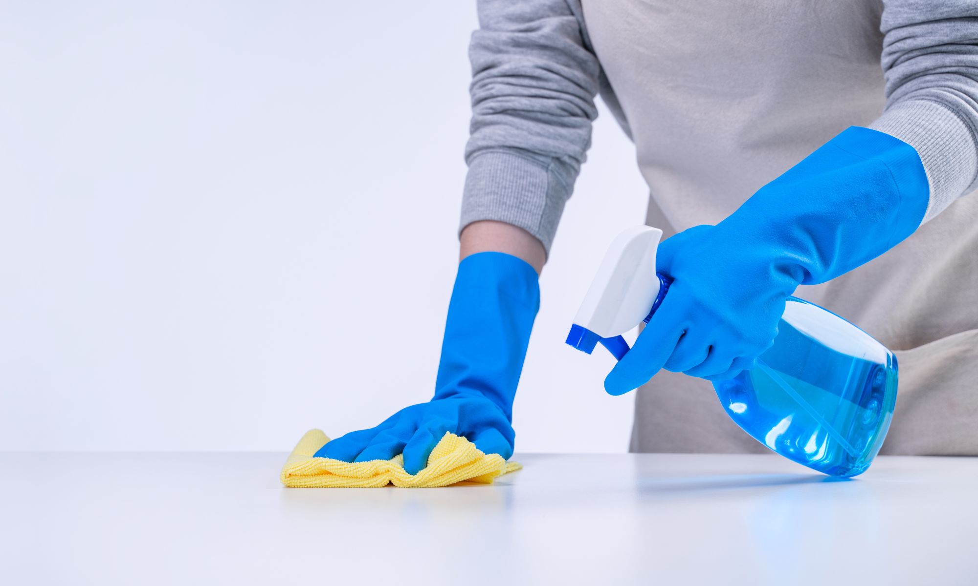 person cleaning surface with gloves and spray bottle